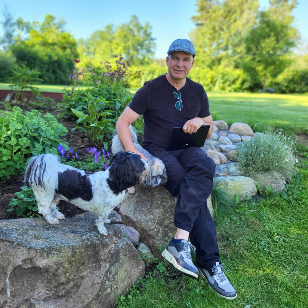 Micke, bostadsbesiktningen, sittandes med sina hundar vid en plantering i trädgården